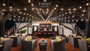 Ampla área de estar com móveis de vime, um bar e uma escadaria que leva aos andares superiores.
