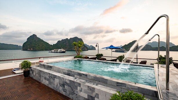 Uma piscina com um elemento aquático, rodeada por um deck de madeira e um muro de pedra.