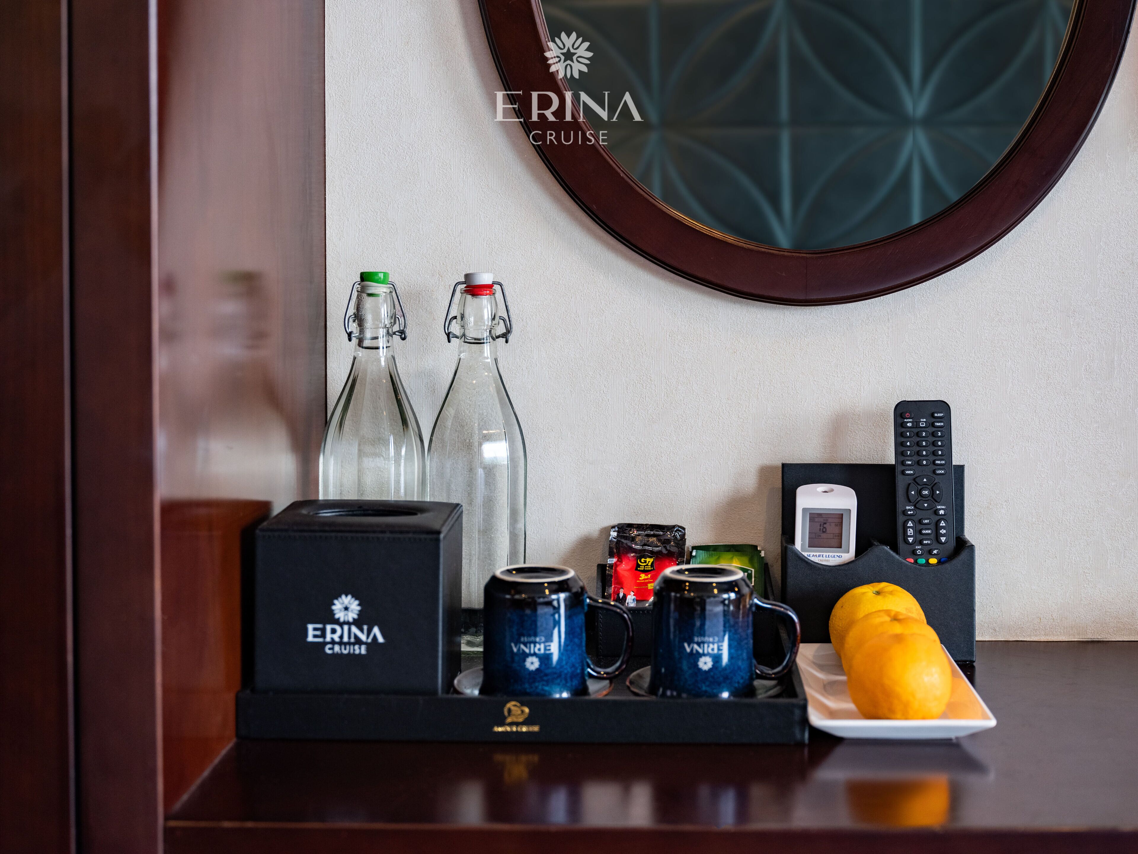 A minibar setup with bottled water, a tea set, a remote control, and a fruit bowl.