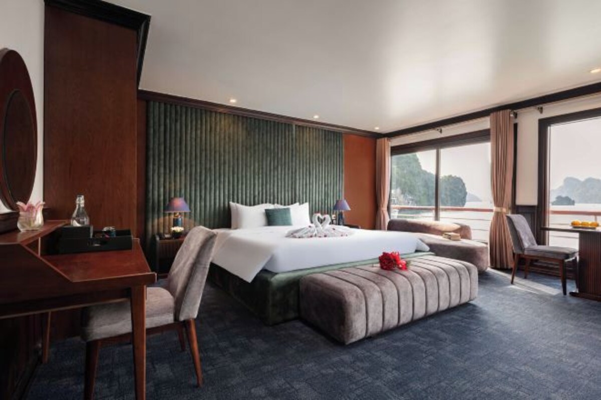 A hotel room with a large bed, a desk, a chair, a small table, and a view of the sea.