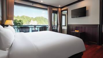 Quarto de hotel com uma cama grande, televisão, varanda com vista para o mar e uma mesa com laranjas.