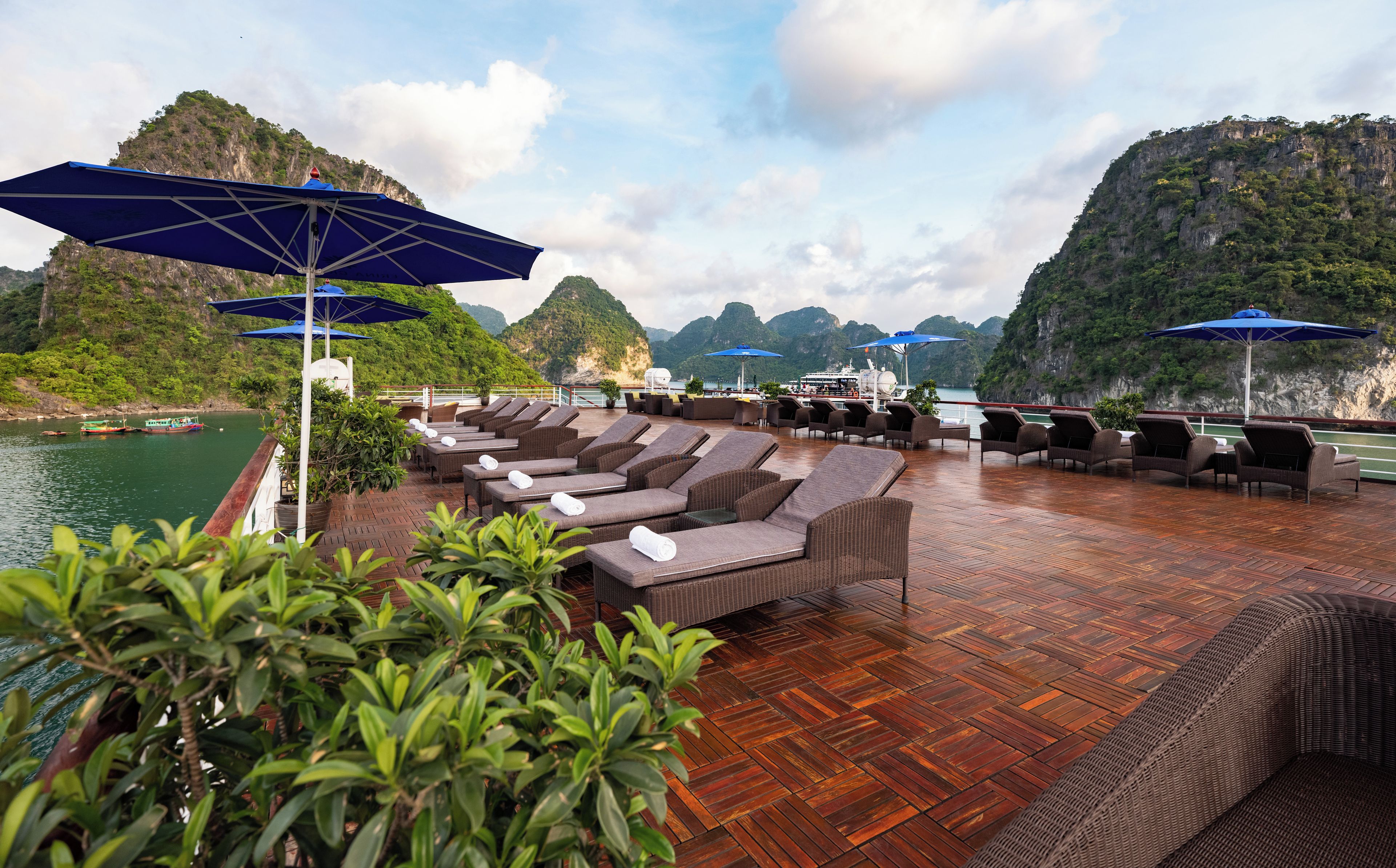 A deck with lounge chairs and umbrellas overlooking a body of water and a mountainous landscape.