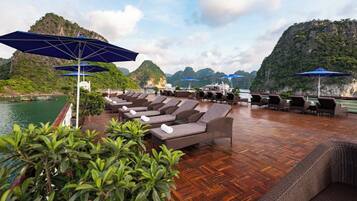 A deck with lounge chairs and umbrellas overlooking a body of water and a mountainous landscape.