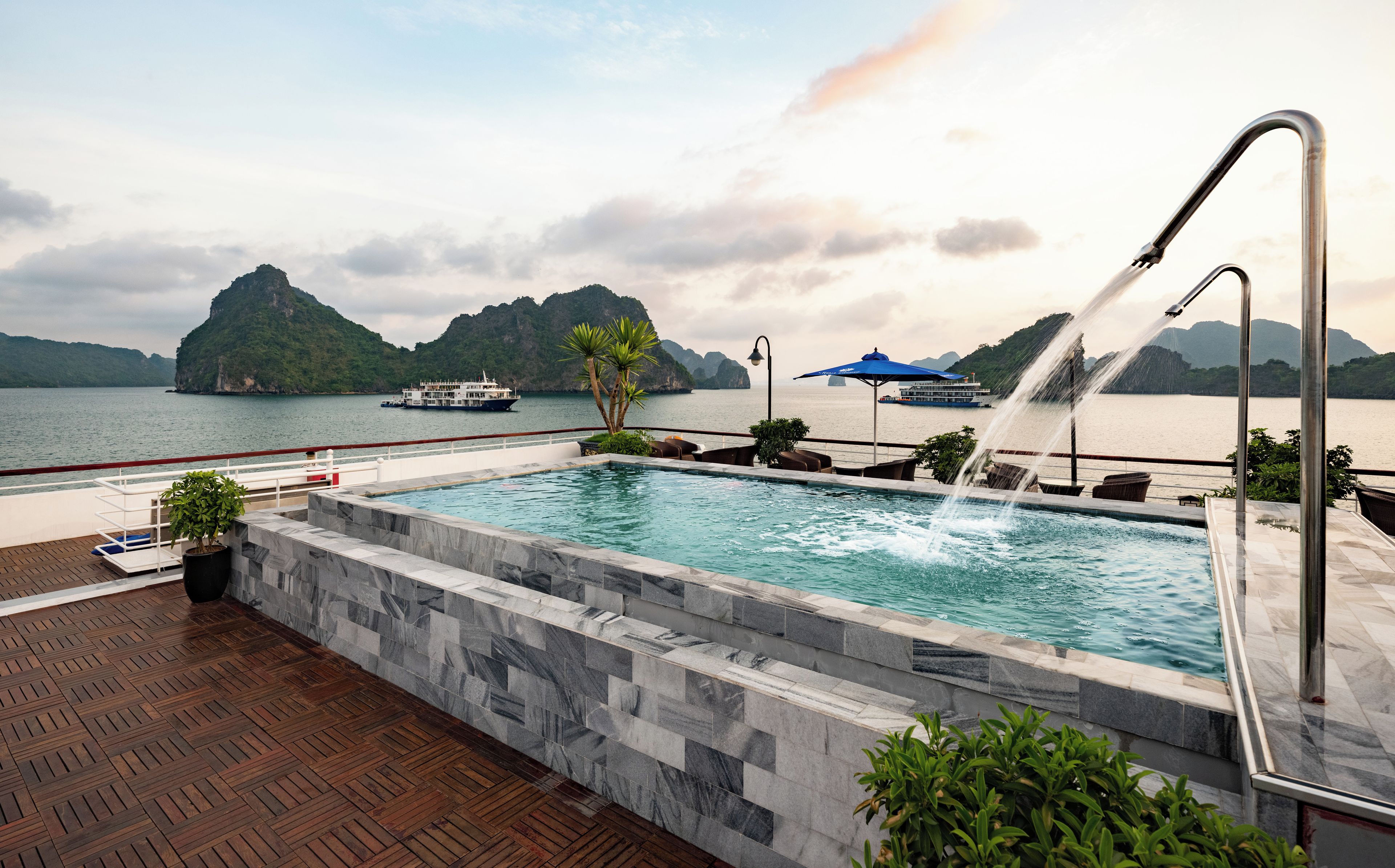 A swimming pool with a water feature, surrounded by a wooden deck and a stone wall.