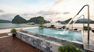 Piscina con fuente, rodeada por una terraza de madera y un muro de piedra.