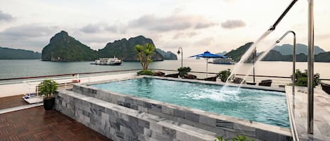 A swimming pool with a water feature, surrounded by a wooden deck and a stone wall.