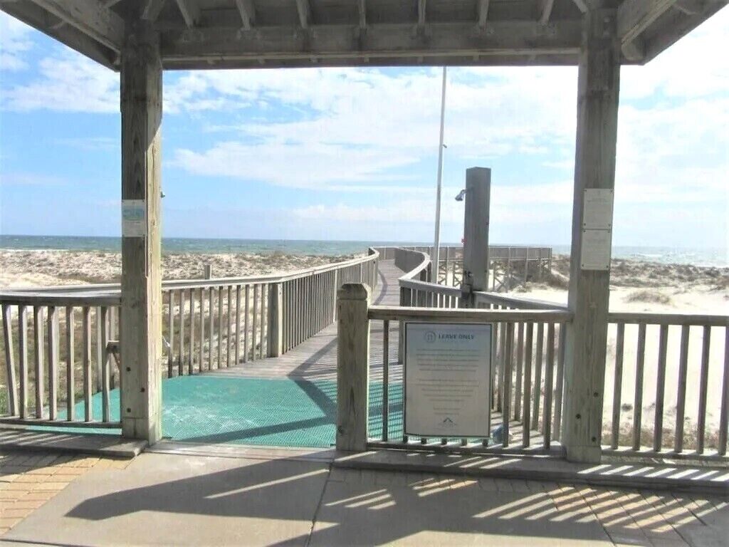 Un pasillo de madera que conduce a una playa, con un letrero que dice 'Leave Only Trash'.