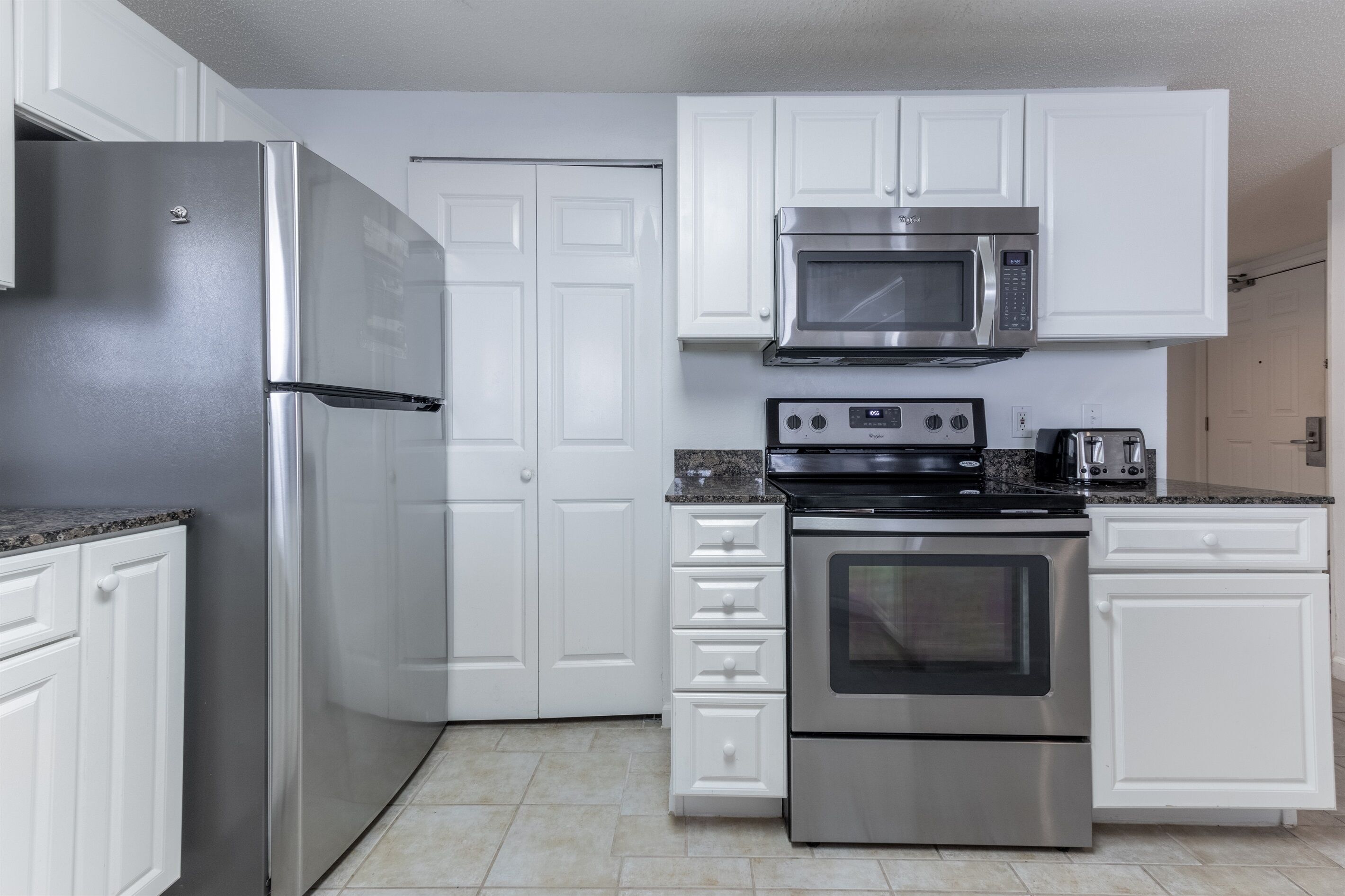 A kitchen with white cabinets, a stainless steel refrigerator, a microwave, a stove, and a toaster.