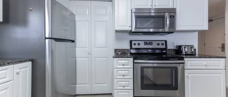A kitchen with white cabinets, a stainless steel refrigerator, a microwave, a stove, and a toaster.