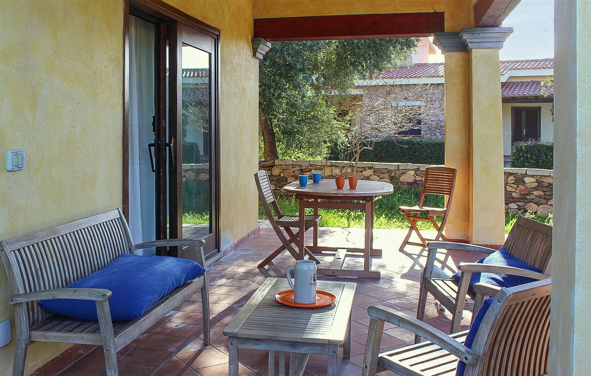 Een terras buiten met een tafel, stoelen, een bank en een stenen muur.