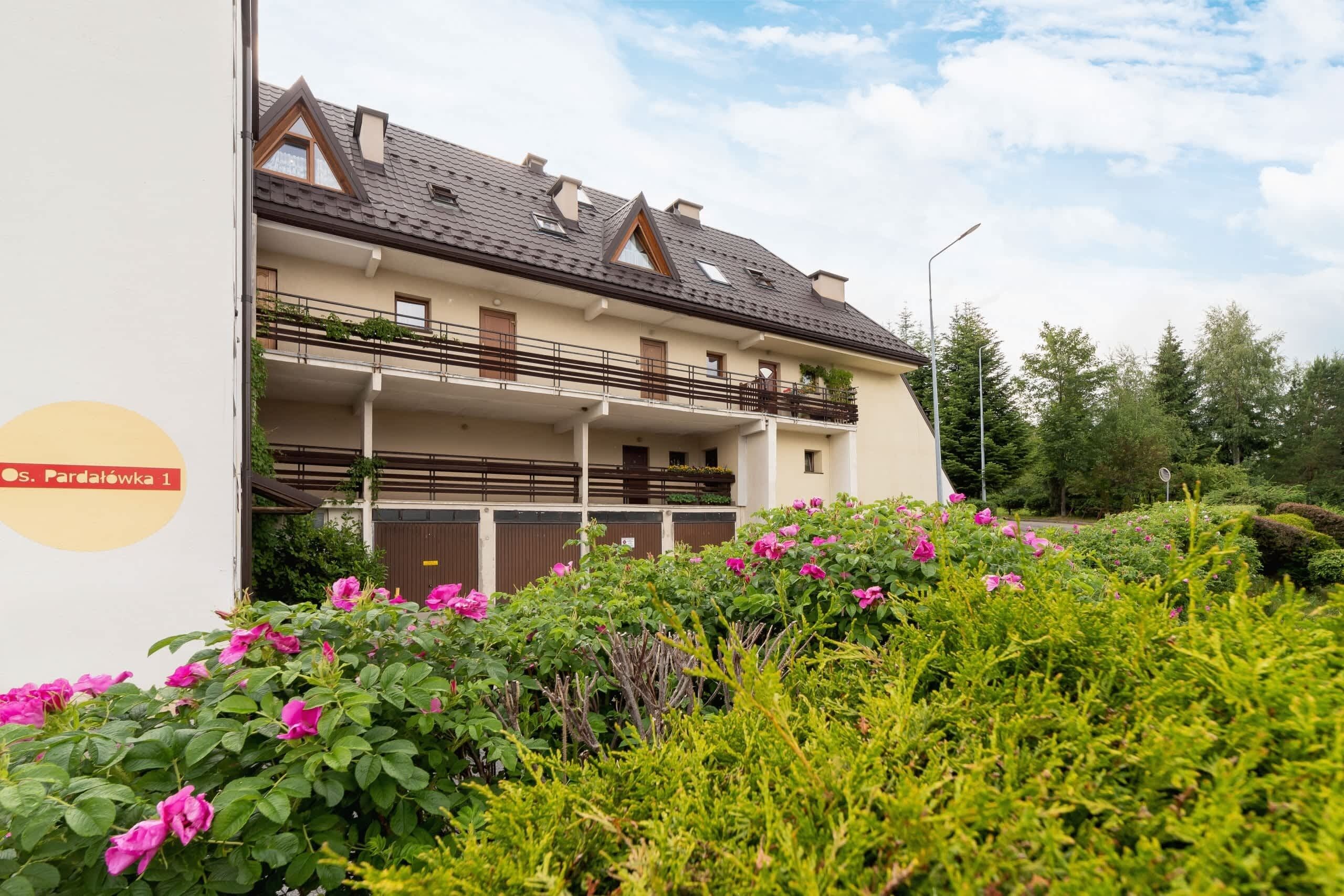 A multi-story residential building with balconies, surrounded by lush greenery and flowering plants.