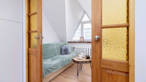 Een gezellige kamer met een houten deur, een groene bank, een klein rond tafeltje en een raam met uitzicht.