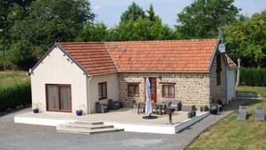 A stone house with a tiled roof, a patio with outdoor furniture, and a gravel driveway. - Light & airy single-storey house with large terrace & heated outdoor pool (Isigny-le-buat)