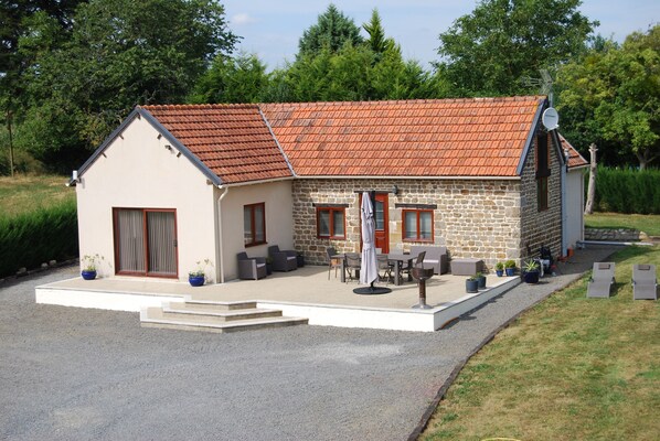 A stone house with a tiled roof, a patio with outdoor furniture, and a gravel driveway.