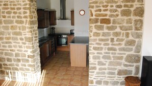A kitchen with stone walls, wooden cabinets, and a tiled floor. - Light & airy single-storey house with large terrace & heated outdoor pool (Isigny-le-buat)