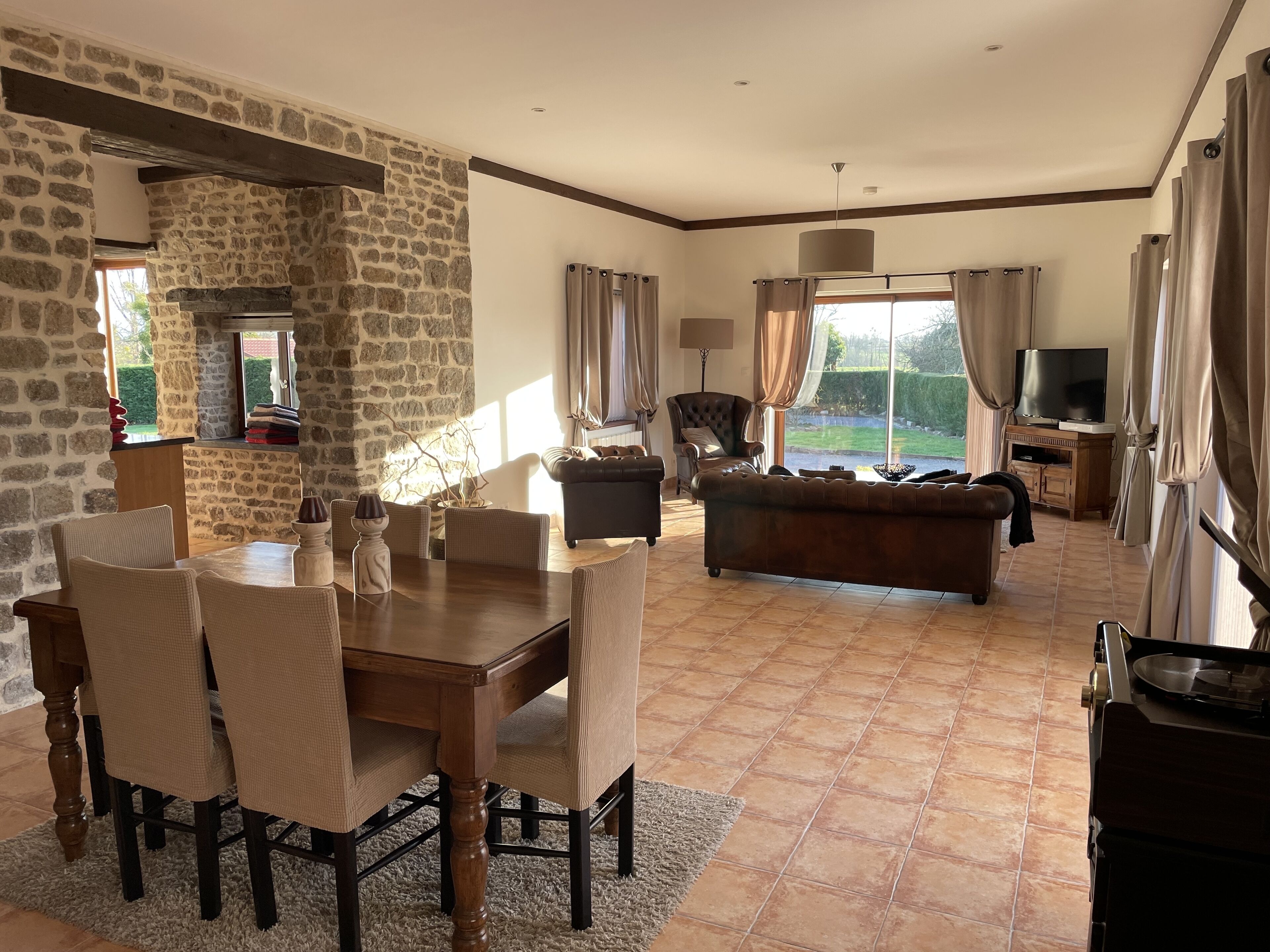 A spacious living room with a stone wall, a dining area with a wooden table and chairs, a leather sofa, and a television.