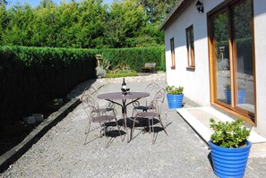 A patio with a round table and chairs, a bottle of wine, and potted plants.