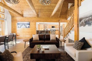 A spacious living area with a wooden ceiling, a sofa set, a coffee table, and a view of the kitchen in the background.