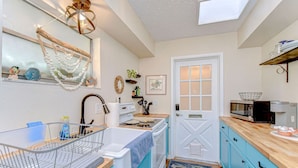 A compact kitchen with a sink, stove, and microwave. There is a window above the sink and a door with frosted glass panels. - Cozy 1BR Retreat w/ Porch – Near Beaches & Airport (Bradenton)