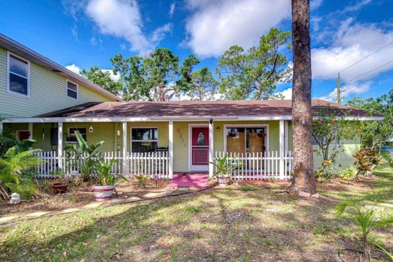 A single-story house with a front porch, a small garden, and a white picket fence.