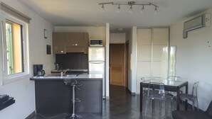 Une cuisine moderne avec un îlot central, un coin repas doté d’une table et de chaises en verre, et un canapé dans l’espace salon.