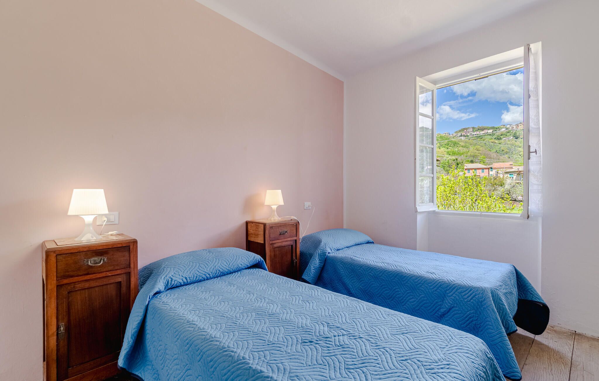 Ein Schlafzimmer mit zwei Betten, einem Fenster mit Blick auf eine hügelige Landschaft und Nachttischen mit Lampen.