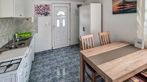 A compact kitchen with a gas stove, a sink, and a refrigerator. There is a dining table with two chairs and a painting on the wall. - Beach front apartment in Vir with WiFi (Vir)