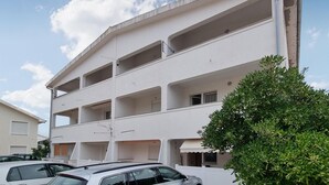 A multi-story building with balconies, a car parked in front, and a tree to the right. - Beach front apartment in Vir with WiFi (Vir)