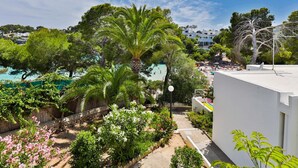A coastal view with a beach, palm trees, and a white building. - 2-Bedroom Holiday Apartment with Beach Access in Cala D'Or (Santanyí)