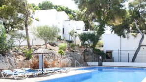 A swimming pool with lounge chairs, a small umbrella, and white buildings in the background. - 2-Bedroom Holiday Apartment with Beach Access in Cala D'Or (Santanyí)
