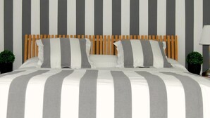 A bed with a striped bedspread and a wooden headboard. There are two small potted plants on either side of the bed. - Hostal Cervantes (Daganzo de Arriba)