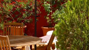 An outdoor patio with a wooden table and chairs, surrounded by potted plants and a climbing plant. - Hostal Cervantes (Daganzo de Arriba)