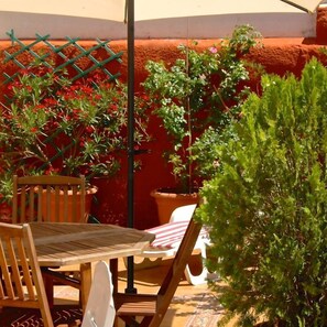 An outdoor patio with a wooden table and chairs, surrounded by potted plants and a climbing plant. - Hostal Cervantes (Daganzo de Arriba)