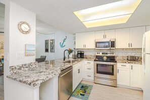 A modern kitchen with white cabinets, a granite countertop, stainless steel appliances, and a ceiling light fixture.