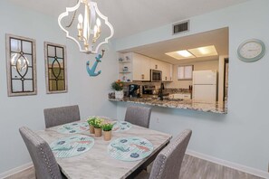 A dining area with a marble table, gray upholstered chairs, decorative wall sconces, and a large mirror reflecting the kitchen.
