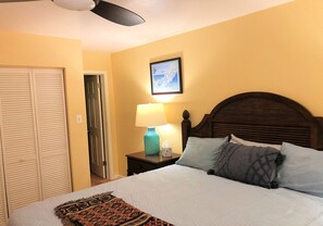 Un dormitorio con cama, una mesita de noche con lámpara, un cuadro enmarcado en la pared y un armario.