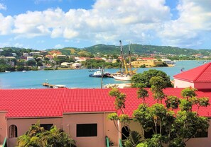 Un pueblo costero con edificios de techo rojo, un puerto deportivo con barcos y un paisaje montañoso de fondo.