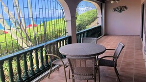 Ein Balkon mit rundem Tisch und Stühlen, Blick aufs Meer und Deckenventilator.