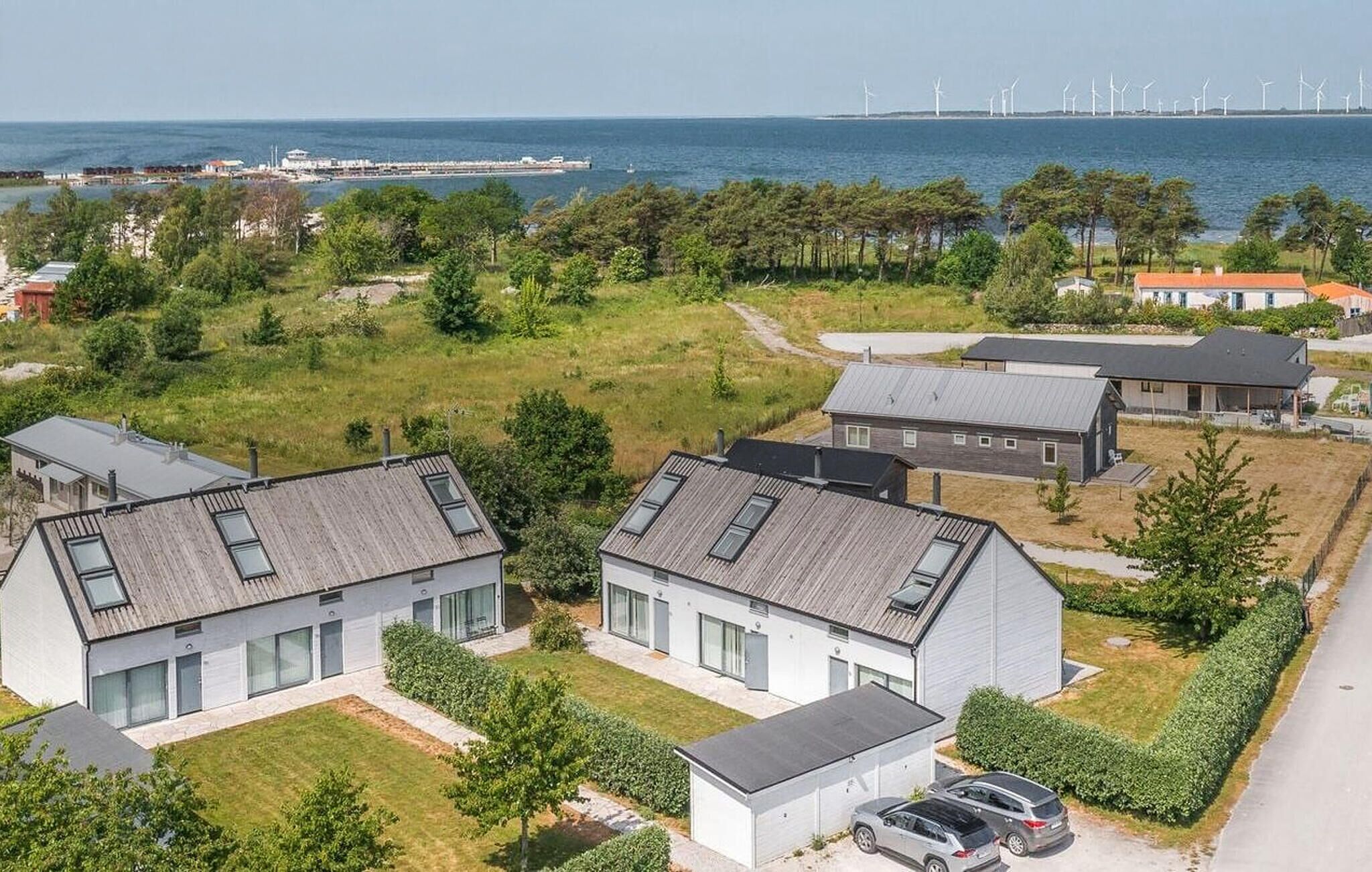 Ett bostadsområde med moderna hus, fri utsikt över havet och vindkraftverk i fjärran.