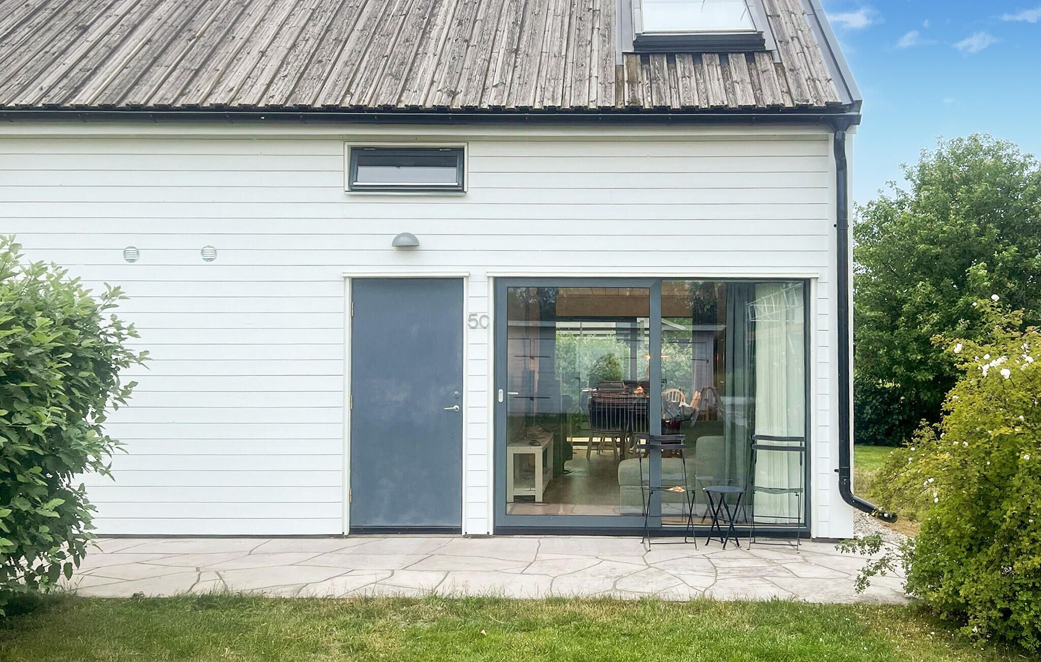 Ett modernt hus med en stor skjutdörr av glas, ett litet fönster och ett tydligt synligt nummer, ”50”, på dörren.