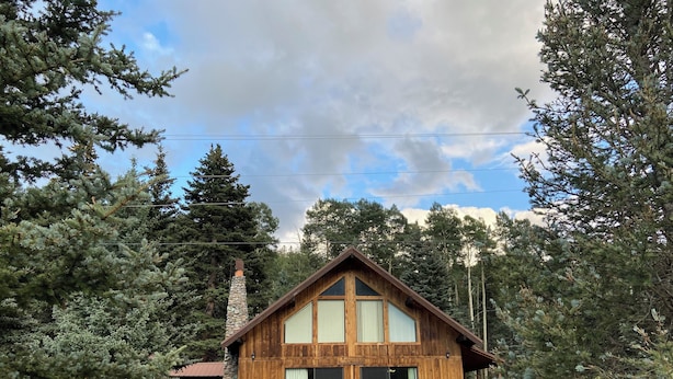 Une cabane en bois avec une cheminée en pierre, de grandes fenêtres et un porche abrité.
