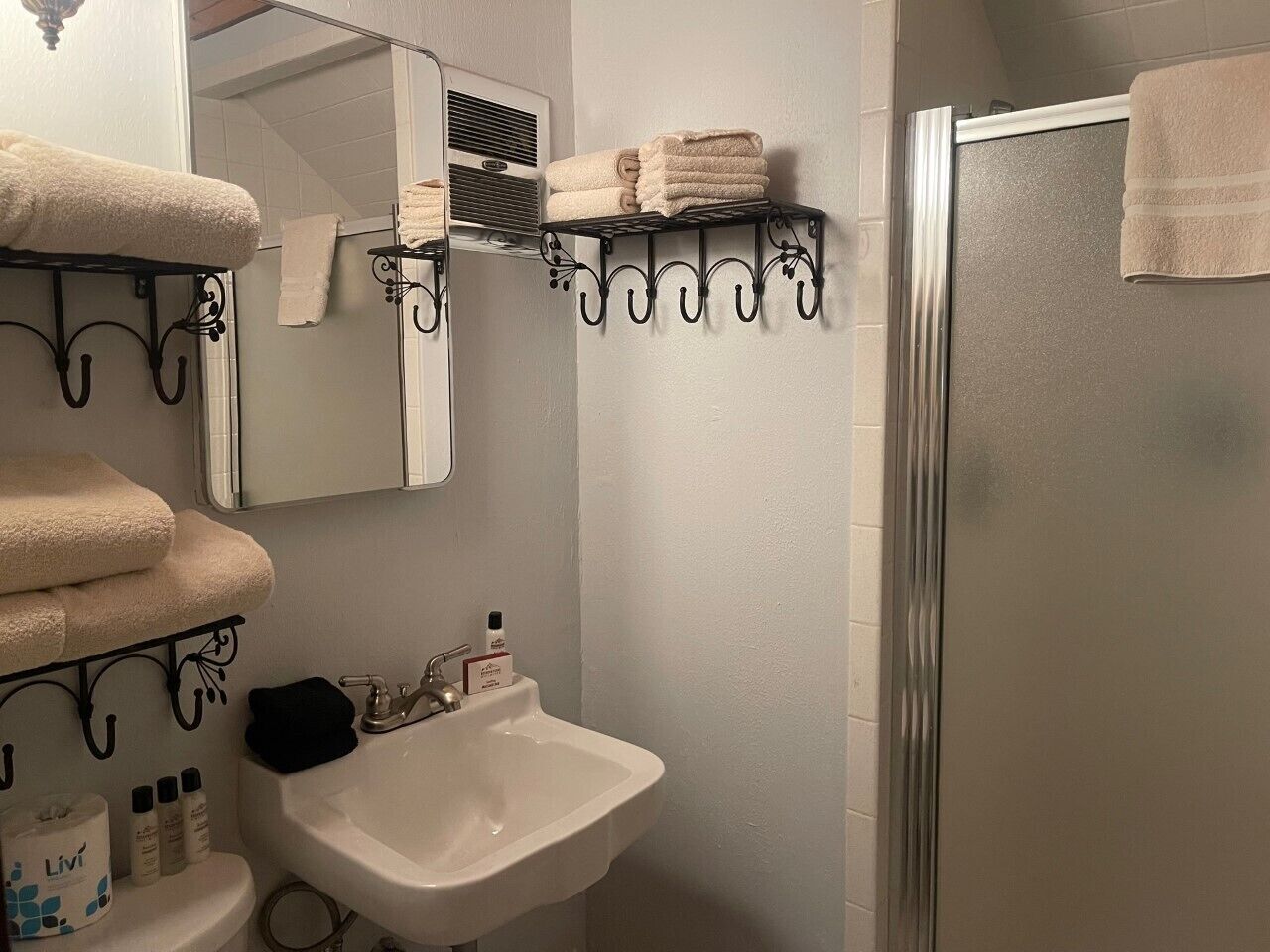 A bathroom with a sink, mirror, towel rack, and shower.