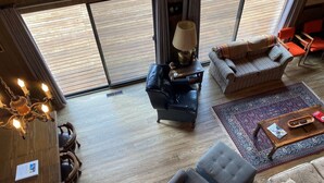 Un vaste espace de vie agrémenté d’une grande fenêtre, d’un lustre, d’un canapé, d’une table basse et d’un tapis à motifs.