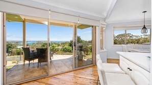 Un interior moderno con un puerta de cristal corrediza que da a un patio exterior, un sofá blanco y un comedor con vista al océano.