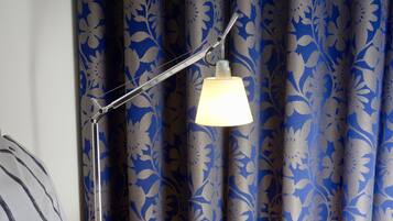 A floor lamp with a white shade and a metal arm, positioned in front of a curtain with a blue floral pattern.