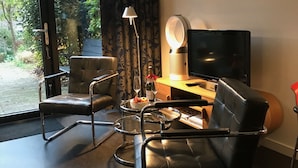 Una sala moderna con una mesa de centro de vidrio, un sofá de cuero negro, un sillón negro, una lámpara de pie, un televisor de pantalla plana y un cuadro con botellas de vino en la pared.