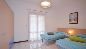 Ein Schlafzimmer mit zwei Betten, einem Nachttisch, einer Lampe, einem Gemälde und einem Fenster mit Vorhängen.