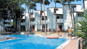 Ein Schwimmbecken mit gefliestem Sonnendeck, umgeben von Bäumen und modernen Gebäuden mit Balkonen.