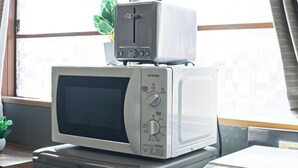 A microwave oven stacked on top of a toaster oven, both placed on a kitchen counter near a window with a view of buildings. - HOME Tengachaya3F (Osaka)