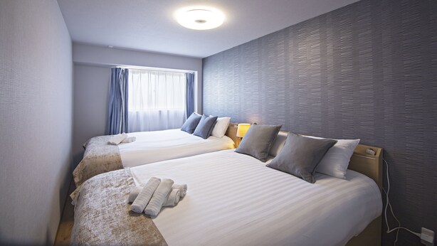 A hotel room with two beds, a window with curtains, a textured wall, and a ceiling light. - HOME Tengachaya3F (Osaka)